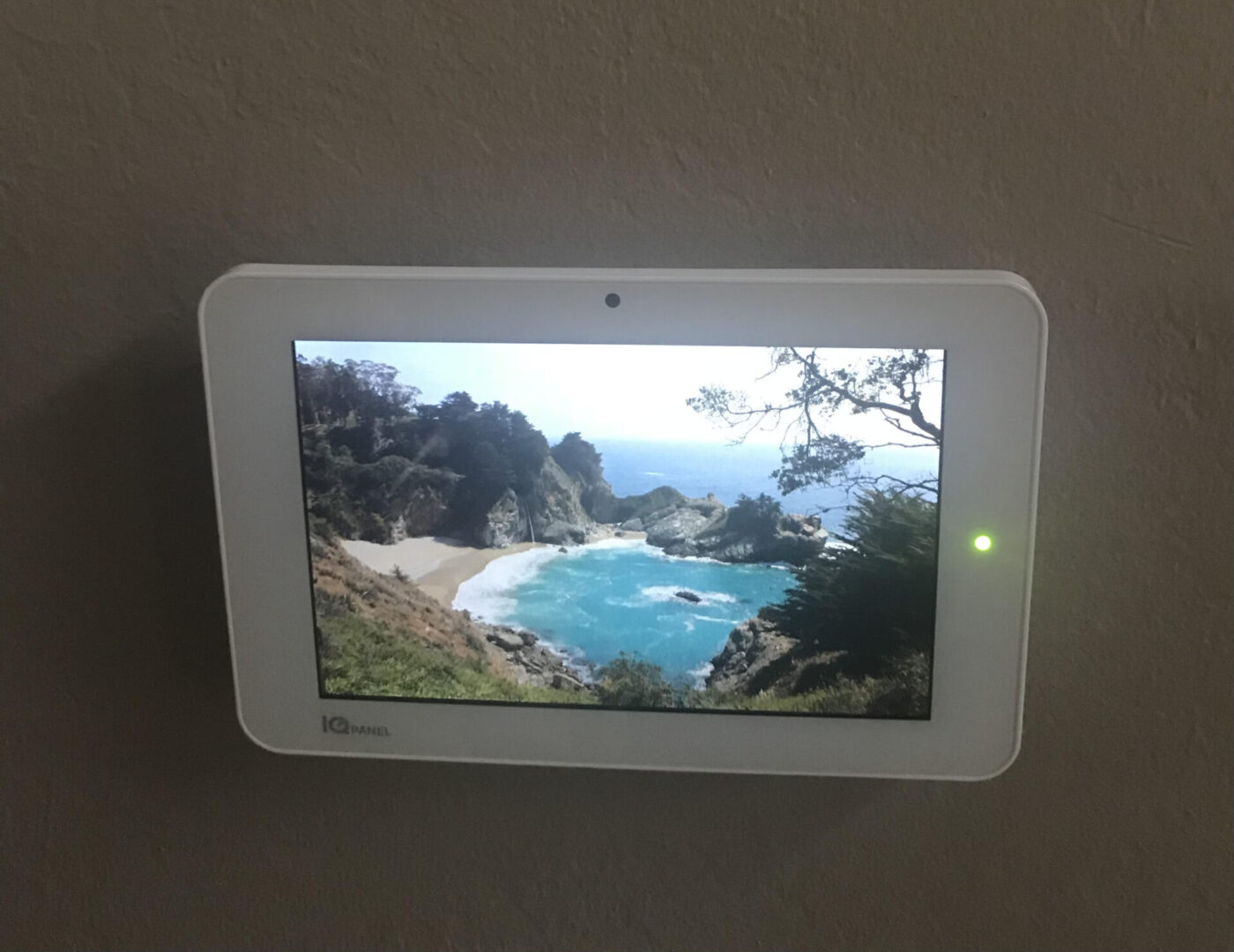 A white tablet mounted on the wall with a green light.